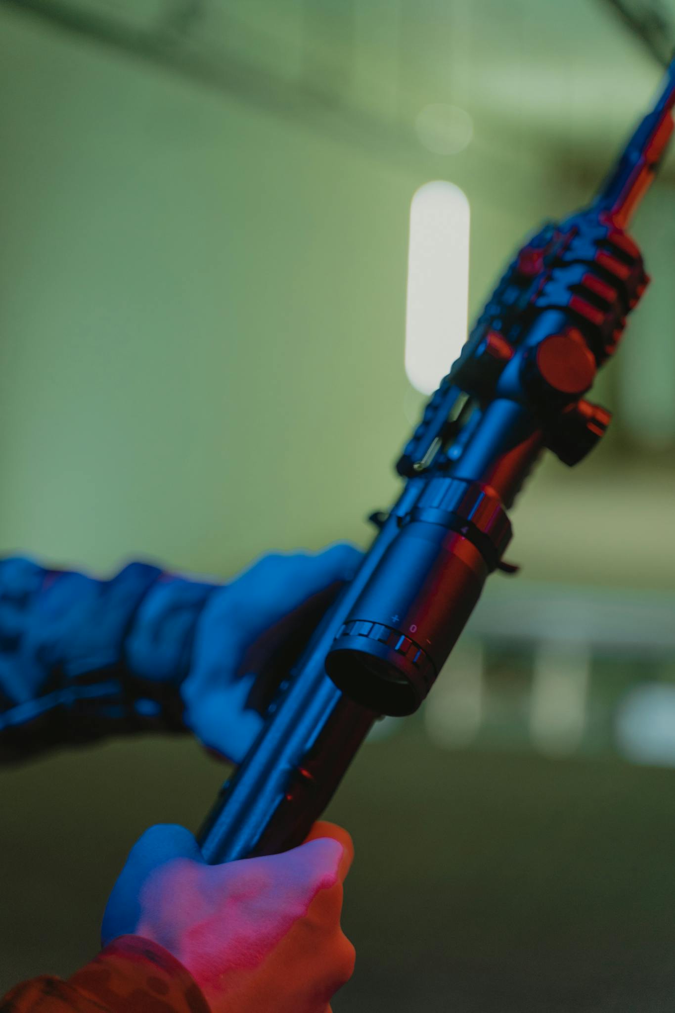 Detailed close-up of a person holding a rifle with a scope in a blurred indoor setting.