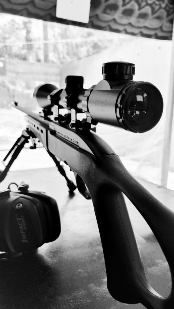 Detailed monochromatic image featuring a scoped rifle on a bipod outdoors.