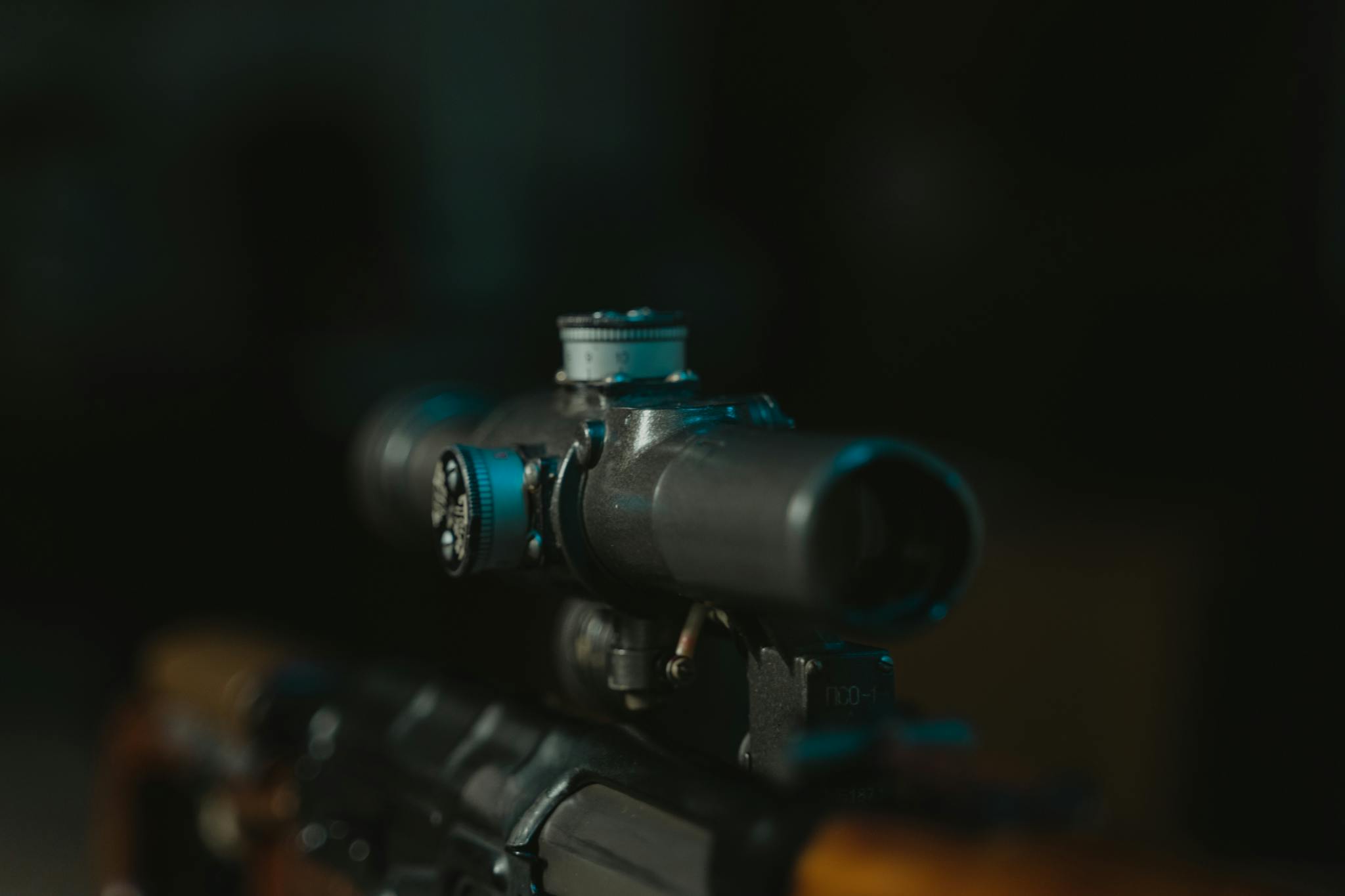 Detailed shot of a rifle scope on a firearm, in low light setting.