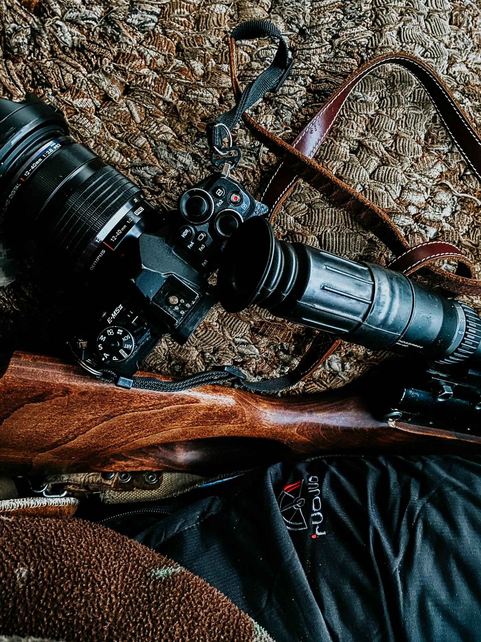 Photography camera and rifle on textured surface, showcasing contrast and detail.